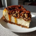 A tempting slice of pecan pie cheesecake with a thick pecan topping and caramel dripping down the side.