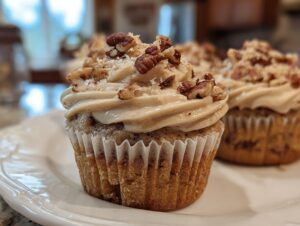 A close-up of a delicious pecan pie cupcake topped with brown sugar frosting and chopped pecans.