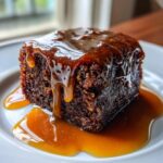 Close-up of a rich, dark square slice of sticky toffee pudding recipe covered in dripping toffee sauce.