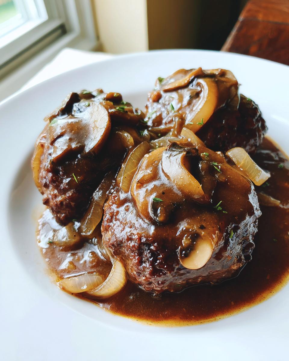 Three servings of rich salisbury steak smothered in brown mushroom and onion gravy on a white plate.