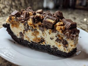 A decadent slice of butterfinger pie featuring a dark chocolate crust, creamy filling, and topped with chopped peanut butter cups.
