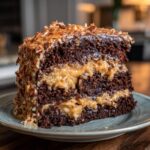 A decadent slice of german chocolate cake showing three layers of dark chocolate cake and coconut-pecan frosting.