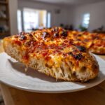Close-up of a thick-crusted slice of homemade pizza showing the airy interior structure and charred tomato topping.