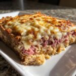 A close-up slice of homemade reuben bake featuring layers of corned beef, sauerkraut, and a thick, melted, golden-brown cheese topping.