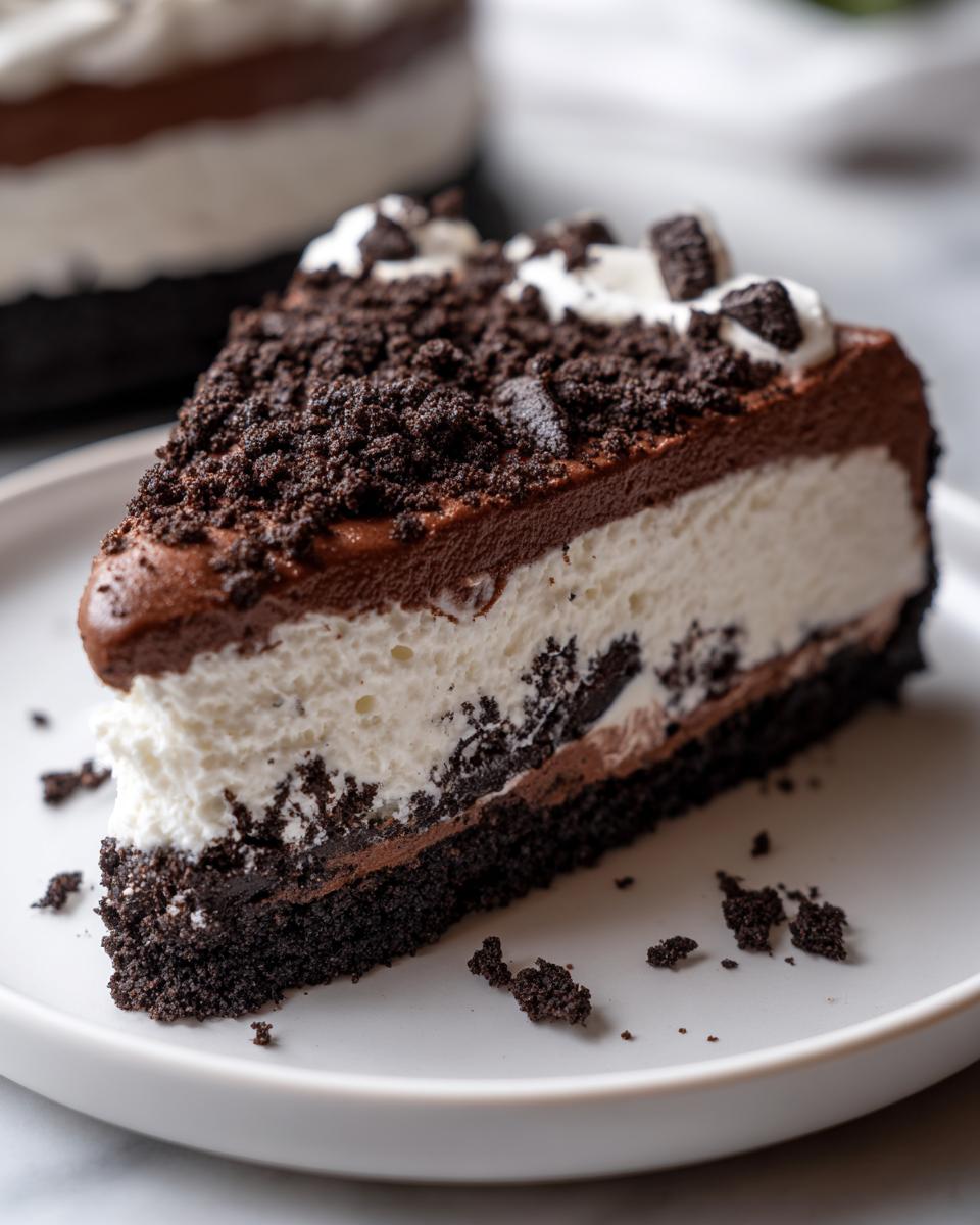 A decadent slice of no bake Oreo pie showing layers of chocolate crust, white cream filling, and chocolate topping, sprinkled with crumbs.