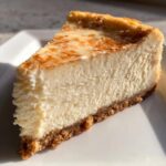 A close-up, appetizing slice of creamy white chocolate cheesecake with a graham cracker crust.