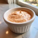 A close-up of creamy, orange-hued smash burger sauce speckled with spices in a small white ramekin.