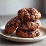 A stack of three rich, dark chocolate pudding cookies featuring gooey, melted chocolate chips.