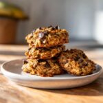 A stack of four homemade breakfast cookie oat clusters loaded with chocolate chips on a light plate.