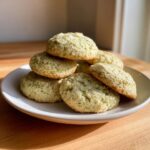 A stack of freshly baked, pale green Earl Grey cookies speckled with tea leaves, resting on a white plate.