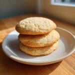 A stack of three golden brown soft sugar cookies resting on a small, light-colored plate.