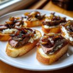 Close-up of several steak crostini appetizers topped with creamy cheese and caramelized onions.