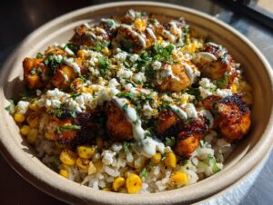 Close-up of a vibrant street corn chicken rice bowl topped with charred chicken, corn, cotija cheese, and a drizzle of crema.