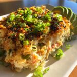 A generous scoop of creamy sushi bake topped with crispy panko, nori flakes, and fresh green onions, served with sliced avocado.
