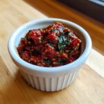 Close-up of thick, vibrant red pizza sauce mixed with herbs in a small white ramekin.