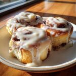 Three freshly baked small batch cinnamon rolls generously topped with thick white icing, sitting on a white plate.