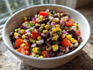 Close-up of a white bowl filled with colorful cowboy caviar featuring black beans, corn, tomatoes, and red onion.