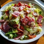 A vibrant, close-up view of a hearty grinder salad featuring crisp lettuce, sliced salami, prosciutto, and shaved Parmesan cheese.