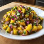 Close-up of a white bowl filled with bright yellow peach salsa, mixed with diced red onion and fresh cilantro.