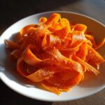 Close-up of bright orange carrot ribbons seasoned with seeds, making a fresh raw carrot salad.