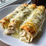 Close-up of three white chicken enchiladas covered in melted white cheese and green herbs.