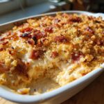 A creamy, baked popper dip with a crispy breadcrumb and bacon topping, showing a scoop taken out.