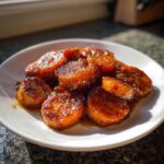 Close-up of thick, glazed slices of amazing candied yams glistening in a sweet syrup on a white plate.