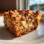 A close-up, sunlit square of apple baked oatmeal showing oats and chunks of apple.
