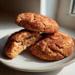 Three soft, thick churro cookies coated in cinnamon sugar, with one cookie broken open to show the chewy interior.