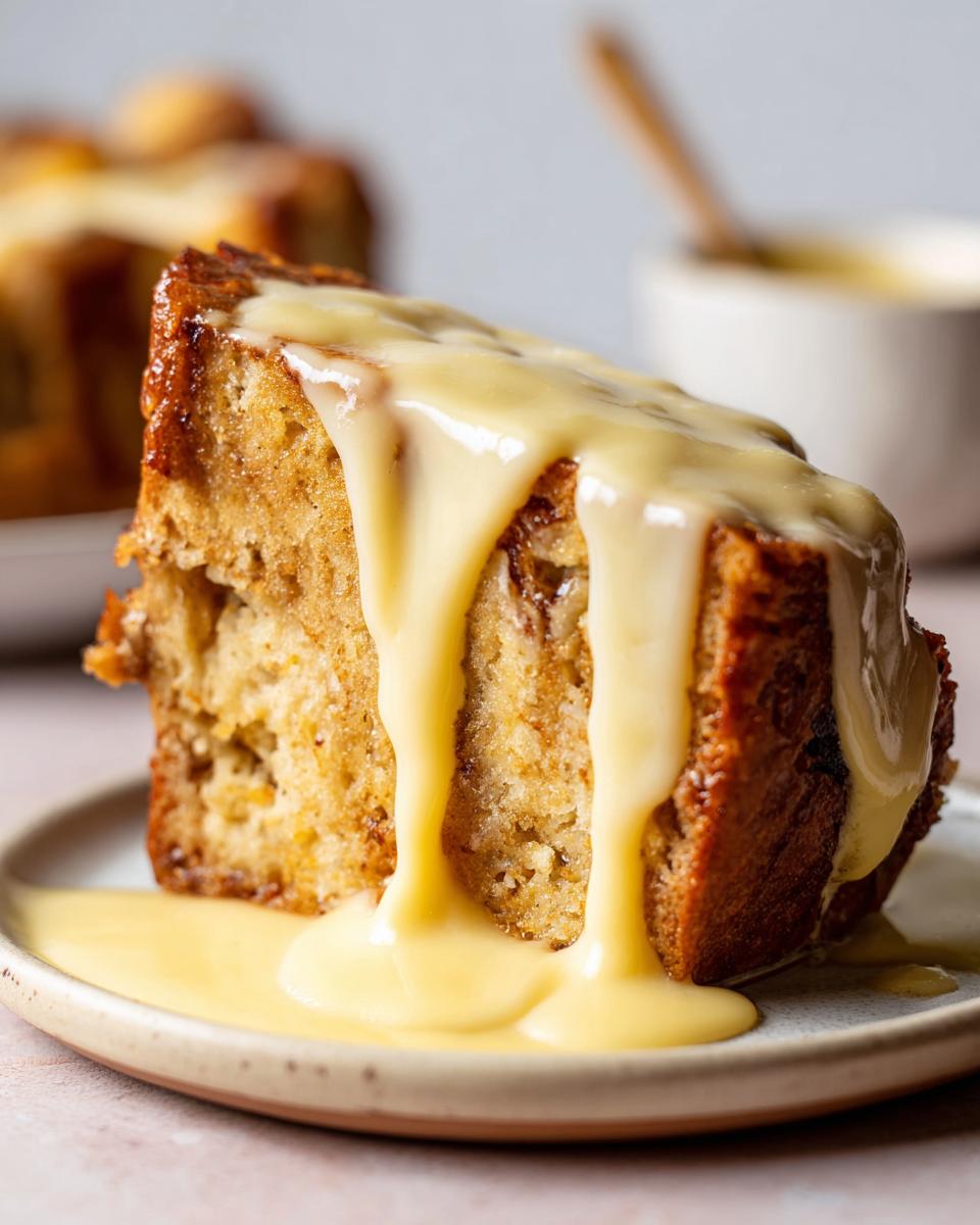 A close-up of a moist slice of bread pudding generously covered in thick, flowing vanilla custard sauce.