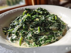 A close-up of rich, dark green creamed spinach served in a white bowl, highlighting the creamy sauce.