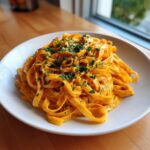 A close-up of creamy butternut squash pasta served on a white plate, topped with chopped fresh parsley.