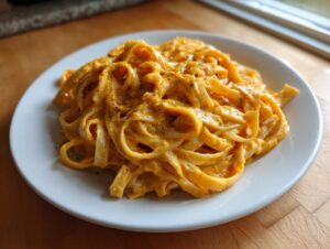 A close-up of creamy butternut squash pasta tossed with fettuccine noodles, seasoned with black pepper.