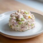 A perfectly scooped mound of creamy ham salad mixed with diced ham and bright green celery pieces, served on a white plate.