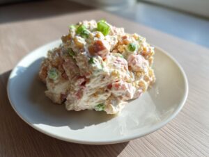 A scoop of creamy ham salad mixed with diced ham and green peas, garnished with green onion, served on a white plate.