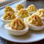 A plate of perfectly piped, creamy deviled eggs dusted with bright red paprika.