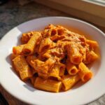 A close-up of rigatoni pasta covered in rich, creamy tomato pasta sauce, sprinkled with cheese.