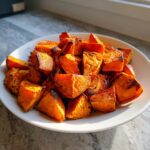 A close-up of perfectly seasoned and crispy roasted sweet potato chunks piled high on a white plate.