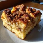 A square slice of fluffy french toast casserole topped with a rich, dark brown cinnamon streusel topping.
