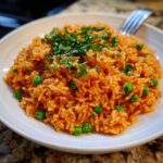 A close-up of fluffy, orange-colored mexican rice mixed with bright green peas and topped with fresh chopped cilantro.