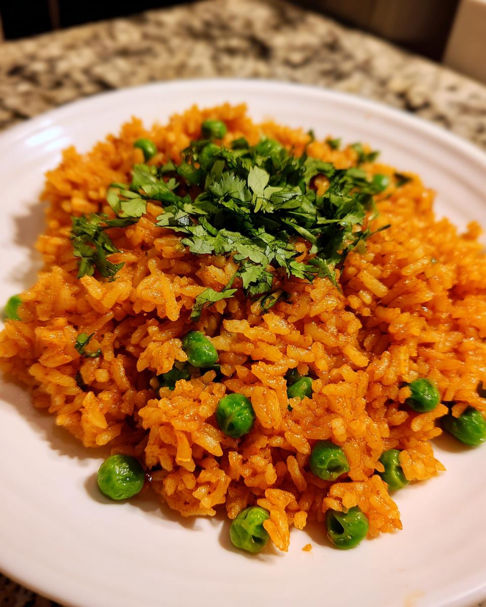 A serving of fluffy Mexican rice recipe, bright orange, mixed with green peas and topped with fresh cilantro.