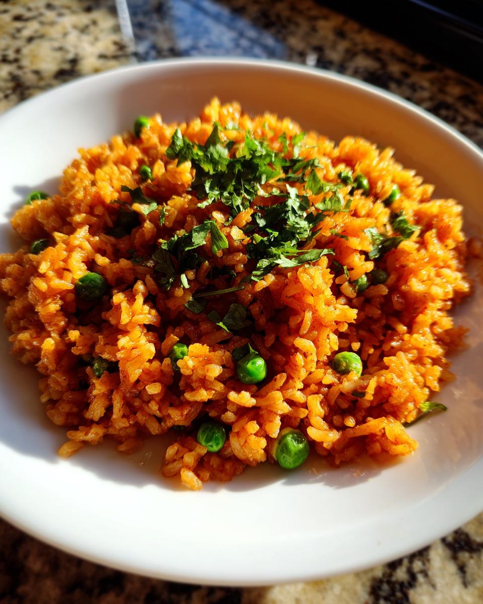 Close-up of fluffy mexican rice recipe, bright orange, mixed with green peas and topped with fresh cilantro.