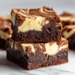 Two stacked, fudgy cheesecake brownies showing a dense chocolate base and a marbled cream cheese swirl topping.