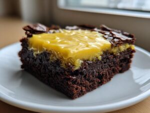 A close-up of a fudgy, dark chocolate Lemon Brownies square topped with a layer of bright yellow lemon curd.