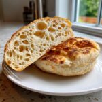 Close-up of homemade english muffins, one sliced to show the open, airy crumb structure.