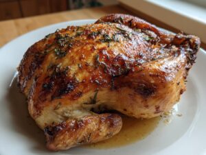 A perfectly roasted whole chicken with golden, crispy skin seasoned with herbs, resting on a white plate.