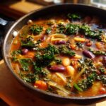 Close-up of rich, steaming minestrone soup in a dark pot, featuring kidney beans, white beans, kale, and vegetables.