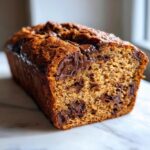 Close-up of a freshly baked, moist chocolate chip banana bread loaf with melted chocolate pockets.