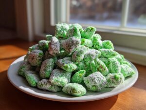 A mound of bright green, powdered sugar-coated pistachio puppy chow piled high on a white plate near a window.