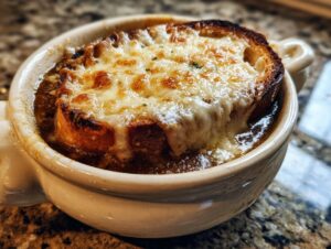 Close-up of a piping hot bowl of french onion soup topped with a thick layer of melted, browned cheese over crouton.